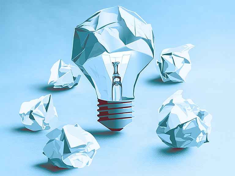 Zu sehen ist ein A.I. von einer Glühbirne bestehend aus zusammengeknülltem Papier, umgeben von anderen zusammengeknüllten Papieren