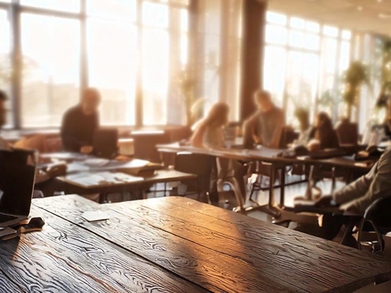 Zu sehen ist ein Gruppenraum mit Erwachsenen die zusammen arbeiten bei abendlichen Sonnenstrahlen durchs Fenster