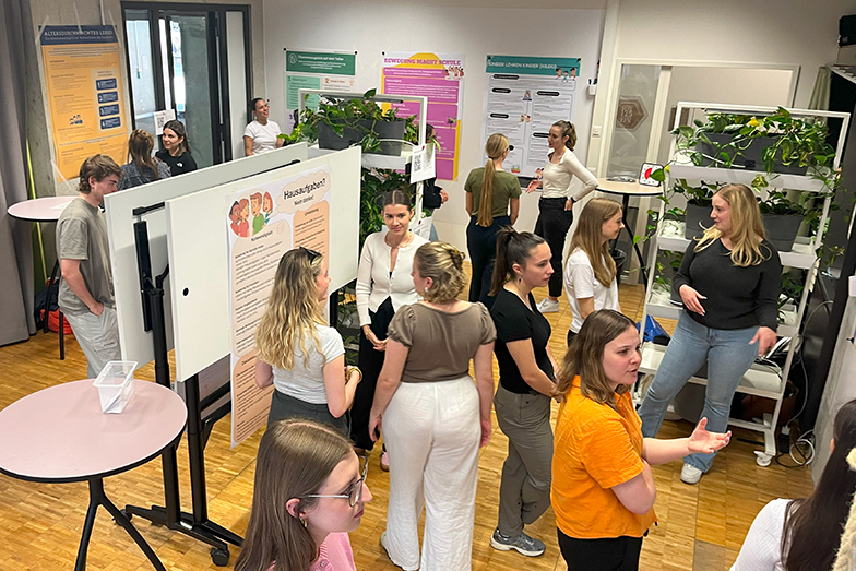 Overview of the room during a poster session. Students are walking around looking at posters and discussing them with each other.