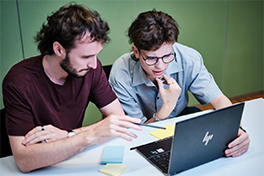 Studierender erklärt seinem Mitstudenten am Laptop seine Arbeit.